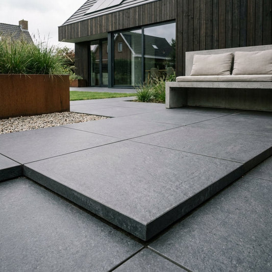 Modern Nederlands terras met grote 60x60 keramische terrastegels op beton, strakke voegen en subtiele tuinbeplanting in zacht daglicht.